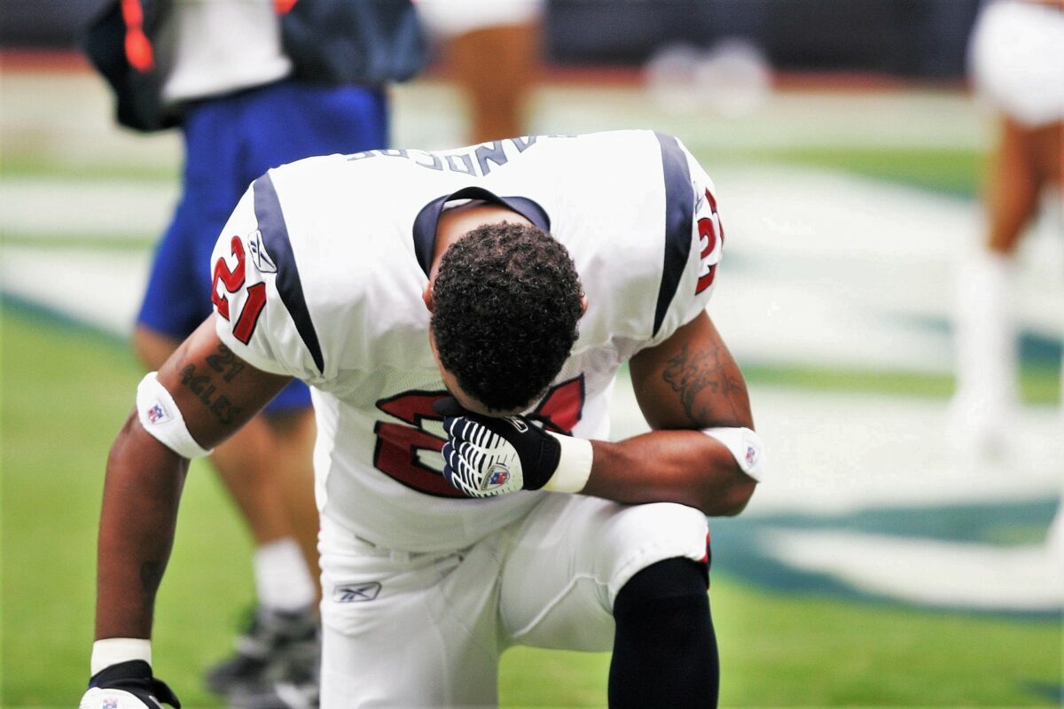 A professional football player kneels on the football field and rests his head on his arm. He feels stress due to the high pressure to perform and is visibly groggy.