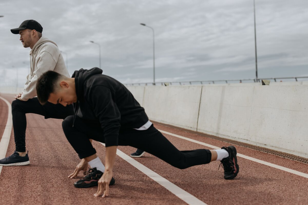 Two men who are stretching on the sports field.