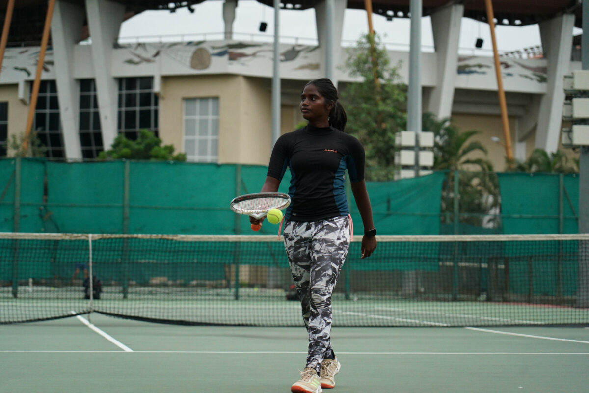 Eine Frau spielt Tennis auf dem Tennisplatz. Sie schlägt den Ball vor ihr auf und macht sich bereit für den Aufschlag. 